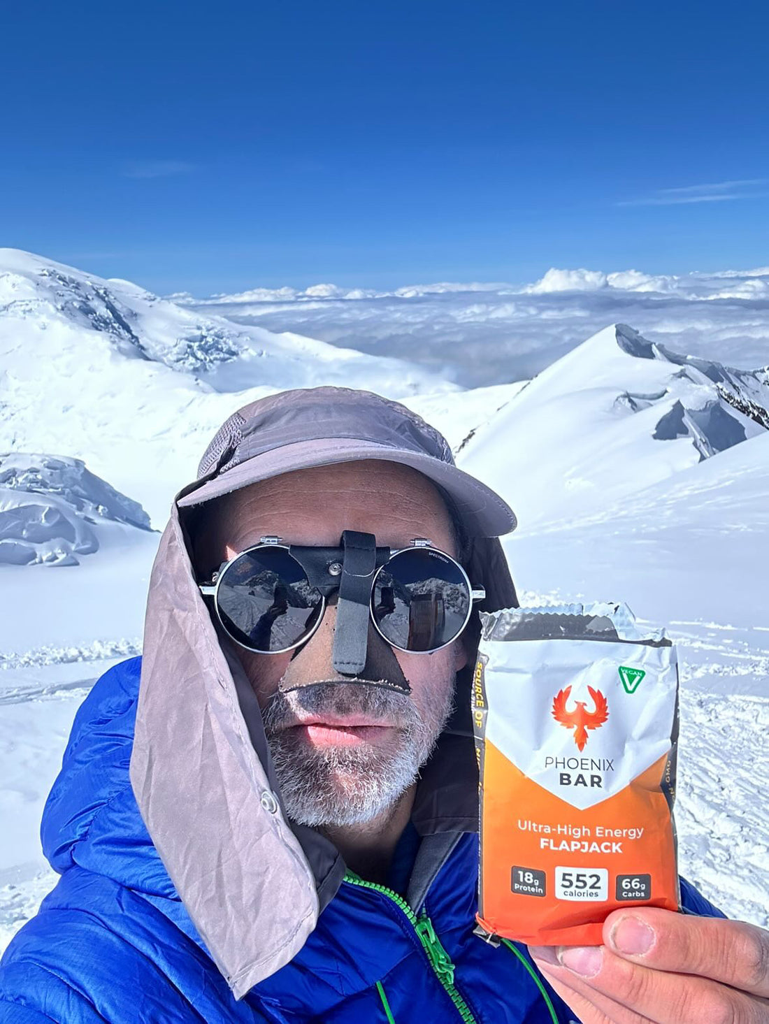 A mountaineer on a snowy summit holding up a Phoenix Bar