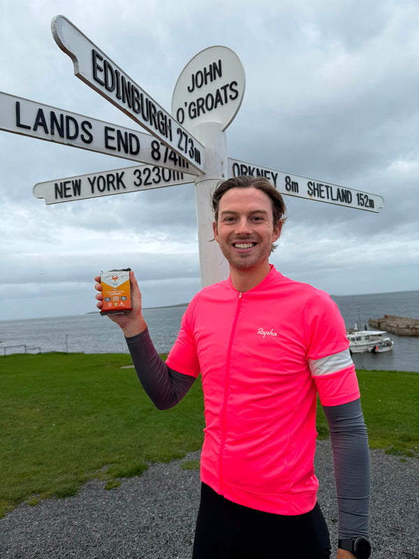 Cyclist at John o' Groats holding a Phoenix Bar